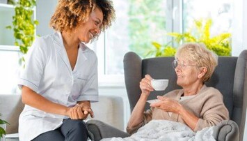 Een zuster drink koffie bij een oudere dame