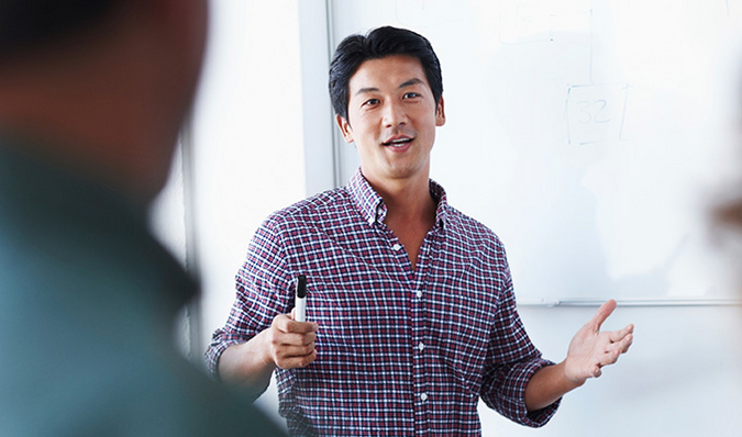 Man in paarse blouse pratend voor een whiteboard